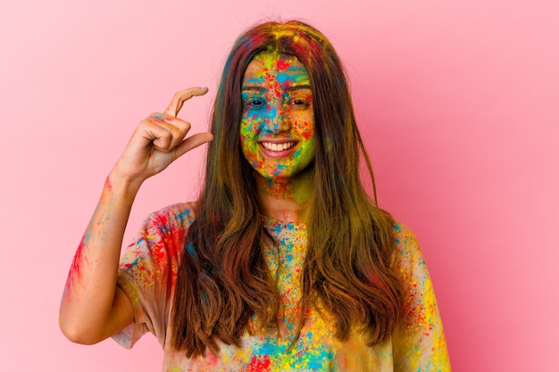 Mulher jovem celebrando o festival sagrado isolado na parede branca segurando algo pequeno com os indicadores, sorrindo e confiante