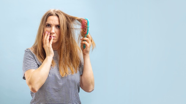 Foto mulher jovem chateada olhando com choque para o cabelo danificado em fundo azul