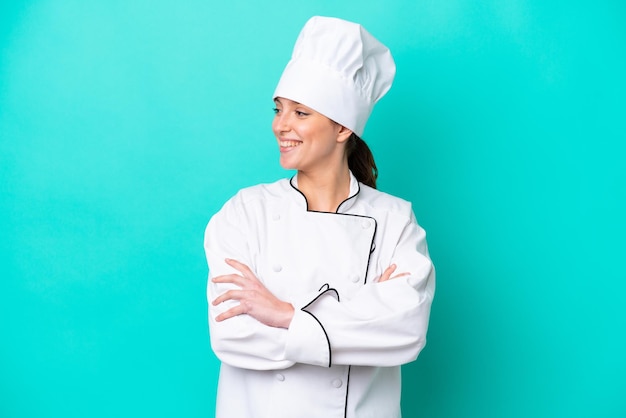Mulher jovem chef caucasiana isolada em fundo azul, olhando de lado