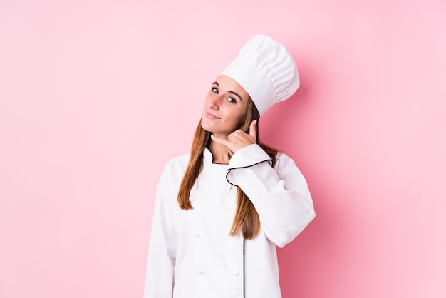 Mulher jovem chef caucasiano mostrando um gesto de chamada de telefone móvel com os dedos.