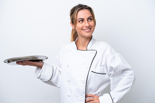 Mulher jovem chef com bandeja isolada no fundo branco, posando com os braços no quadril e sorrindo