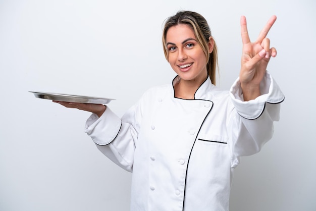 Mulher jovem chef com bandeja isolada no fundo branco sorrindo e mostrando sinal de vitória