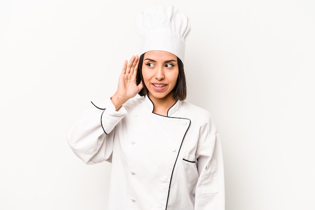 Mulher jovem chef hispânico isolada no fundo branco tentando ouvir uma fofoca