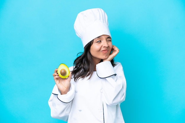 Mulher jovem chef hispânico segurando abacate isolado em fundo azul frustrado e cobrindo as orelhas