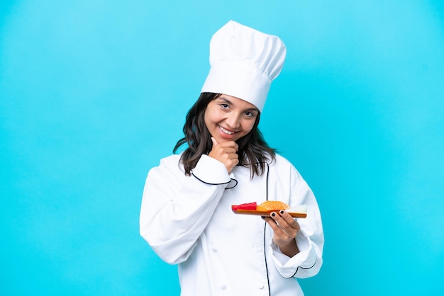 Mulher jovem chef hispânico segurando sashimi isolado em fundo azul feliz e sorridente