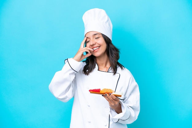 Mulher jovem chef hispânico segurando sashimi isolado no fundo azul sorrindo muito