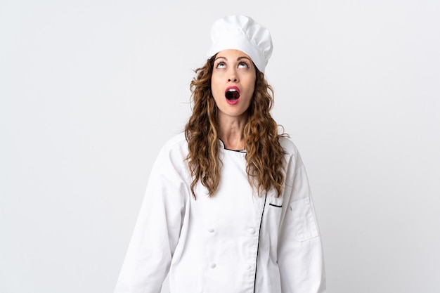 Mulher jovem chef isolada no fundo branco, olhando para cima e com expressão de surpresa