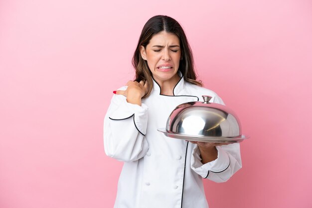 Mulher jovem chef italiano segurando a bandeja com tampa isolada no fundo rosa, sofrendo de dor no ombro por ter feito um esforço