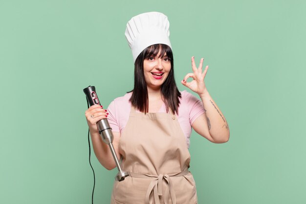 Mulher jovem chef se sentindo feliz, relaxada e satisfeita, mostrando aprovação com um gesto de ok, sorrindo