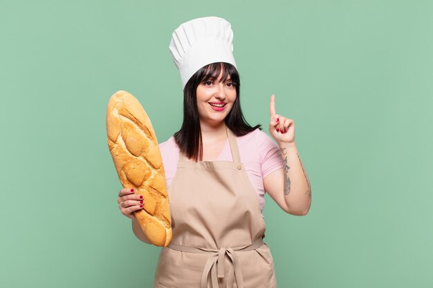 Mulher jovem chef sorrindo e parecendo amigável, mostrando o número um ou primeiro com a mão para a frente, em contagem regressiva