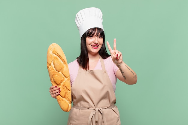 Mulher jovem chef sorrindo e parecendo feliz, despreocupada e positiva, gesticulando vitória ou paz com uma mão