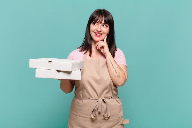 Mulher jovem chef sorrindo feliz e sonhando acordada ou duvidando, olhando para o lado