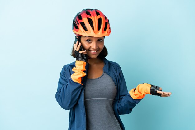 Foto mulher jovem ciclista isolada em fundo azul, conversando com alguém ao telefone celular