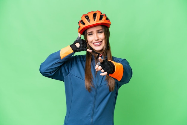 Mulher jovem ciclista sobre fundo croma chave isolado fazendo gesto de telefone e apontando para a frente