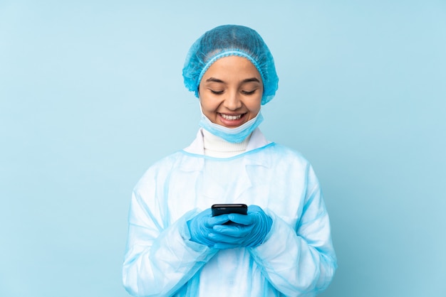 Mulher jovem cirurgião de uniforme azul, enviando uma mensagem com o celular