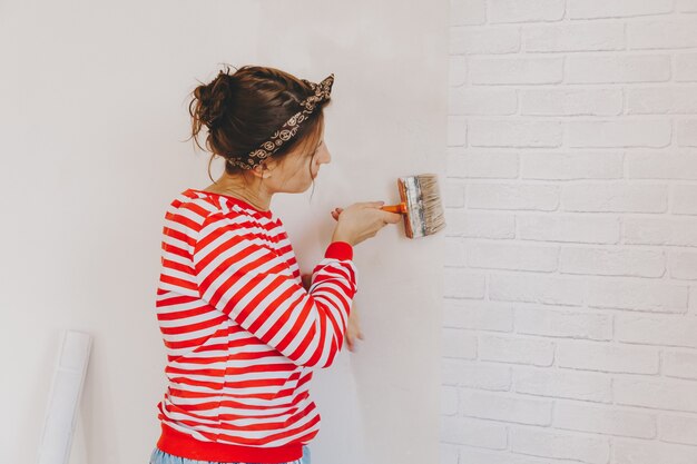 Mulher jovem cola papel de parede em casa. garota cola papel de parede na forma de um tijolo. reparar.