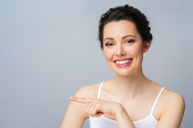 Foto mulher jovem com aparelho nos dentes rindo e apontando com a mão para o espaço da cópia