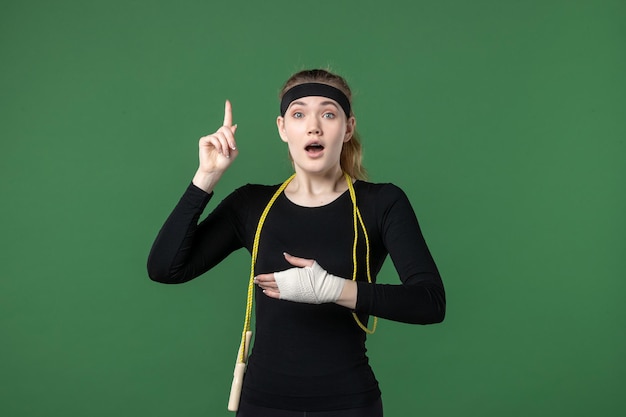 Mulher jovem com bandagem em volta do braço machucado, em fundo verde, vista frontal, atleta, dor, mulher, treino, corpo, cores, ferimento, saúde