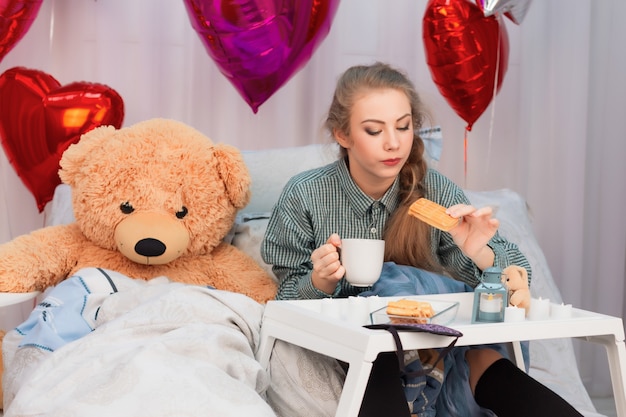 Mulher jovem com cabelo comprido tomando café da manhã na cama no Dia dos Namorados