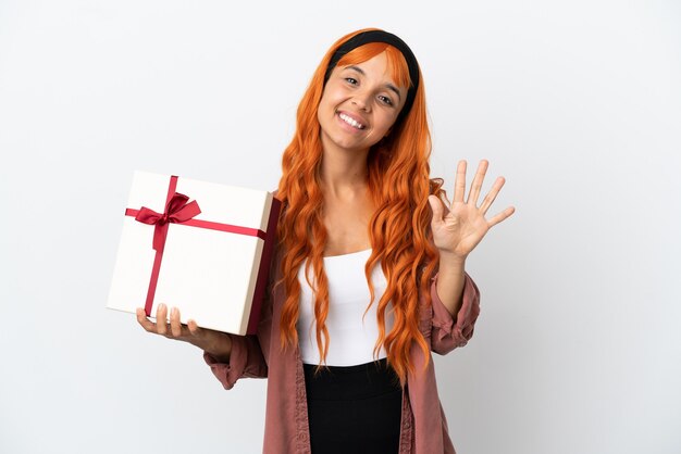 Mulher jovem com cabelo laranja segurando um presente isolado no fundo branco, contando cinco com os dedos