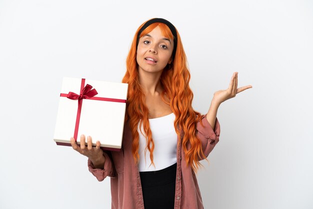 Mulher jovem com cabelo laranja segurando um presente isolado no fundo branco, estendendo as mãos para o lado para convidar para vir