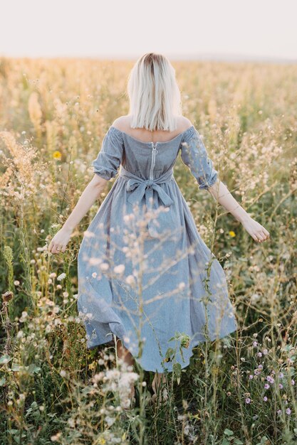 Mulher jovem com cabelo loiro em pé em um campo com um vestido azul