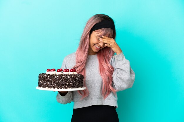 Mulher jovem com cabelo rosa segurando um bolo de aniversário isolado em um fundo azul rindo