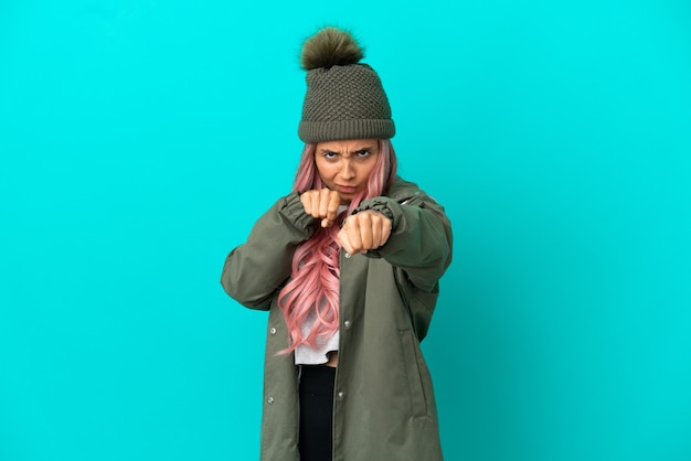 Foto mulher jovem com cabelo rosa vestindo um casaco à prova de chuva isolado em um fundo azul com gesto de luta