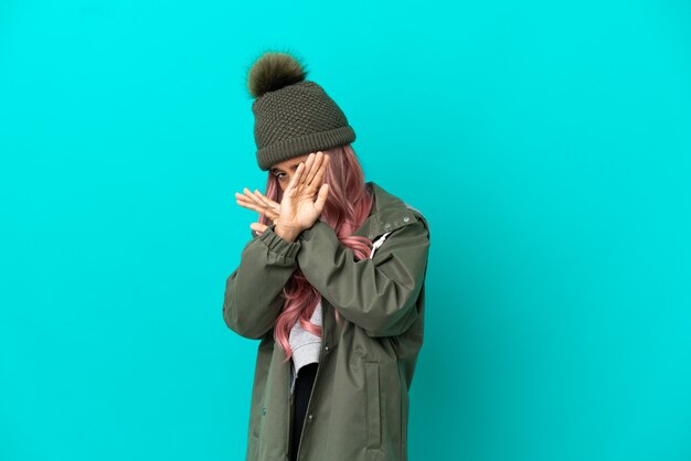 Foto mulher jovem com cabelo rosa vestindo um casaco à prova de chuva isolado em um fundo azul nervosa esticando as mãos para a frente