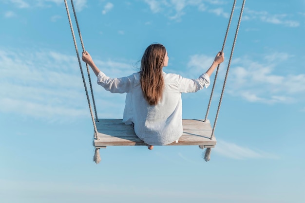 Mulher jovem com cabelos longos em balanço alto no ar em meio ao fundo do céu azul vista de trás conceito de liberdade e leveza