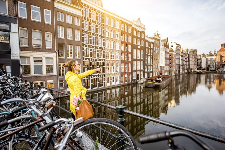 Foto mulher jovem com capa de chuva amarela apreciando a vista matinal na bela vista da cidade em amsterdã
