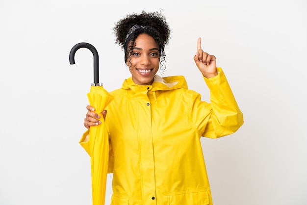 Mulher jovem com casaco à prova de chuva e guarda-chuva isolado no fundo branco apontando para uma ótima ideia