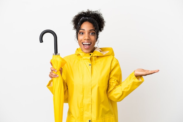 Mulher jovem com casaco à prova de chuva e guarda-chuva isolado no fundo branco com expressão facial chocada