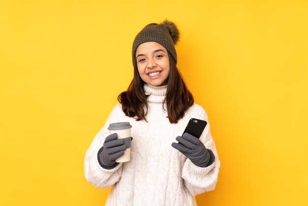 Mulher jovem com chapéu de inverno isolada segurando um café para levar e um móbile