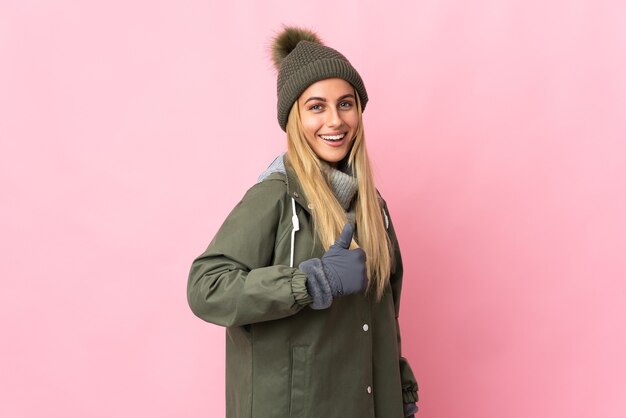 Mulher jovem com chapéu de inverno isolado em uma parede rosa fazendo um gesto de polegar para cima