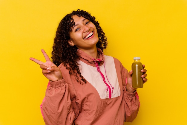 Mulher jovem com esporte de raça mista segurando um smoothie isolado em amarelo