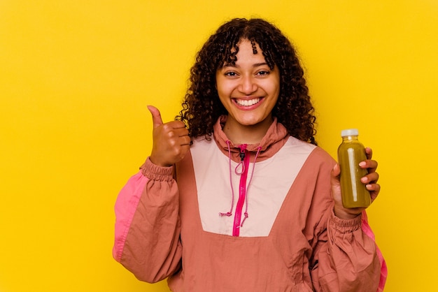 Mulher jovem com esporte de raça mista segurando um smoothie isolado em um fundo amarelo