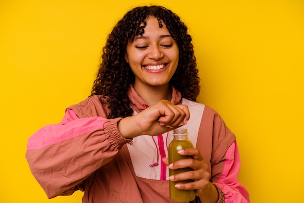 Mulher jovem com esporte de raça mista segurando um smoothie isolado na parede amarela