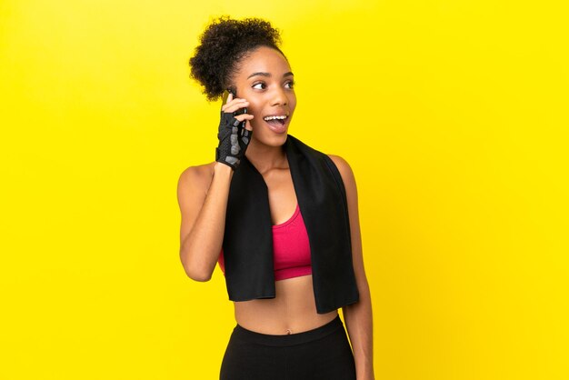 Mulher jovem com esportes africanos isolada em um fundo amarelo, conversando com o telefone celular.