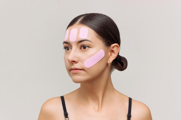 Foto mulher jovem com fita kinesio rosa no rosto para reduzir rugas e apertar o oval do rosto
