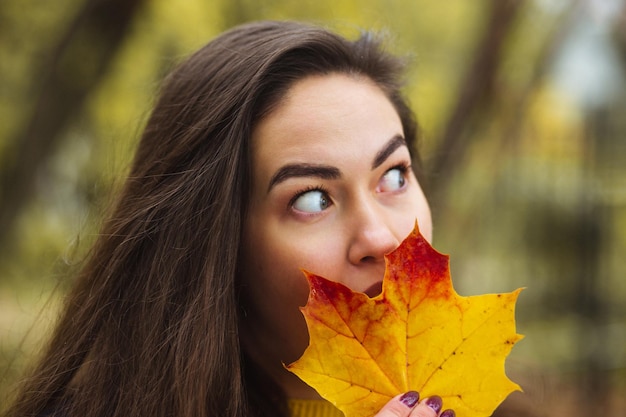 Mulher jovem com folhas de outono na mão e fundo de jardim de bordo amarelo outono