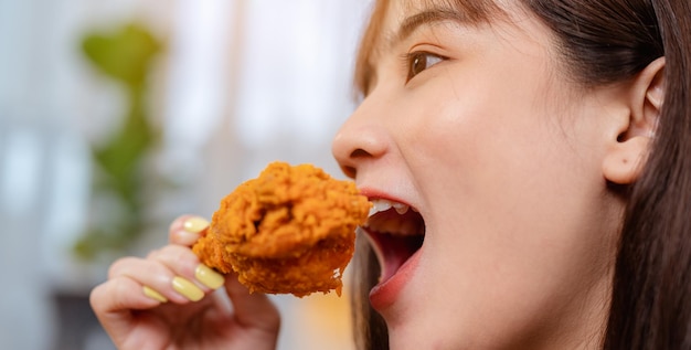 Mulher jovem com fome comendo junk food, frango frito e batatas fritas no almoço, pedindo entrega, relaxando em casa nas férias. refeição não saudável, risco de obesidade.