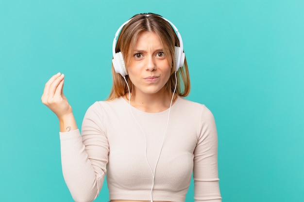 Mulher jovem com fones de ouvido fazendo capice ou gesto de dinheiro, dizendo para você pagar