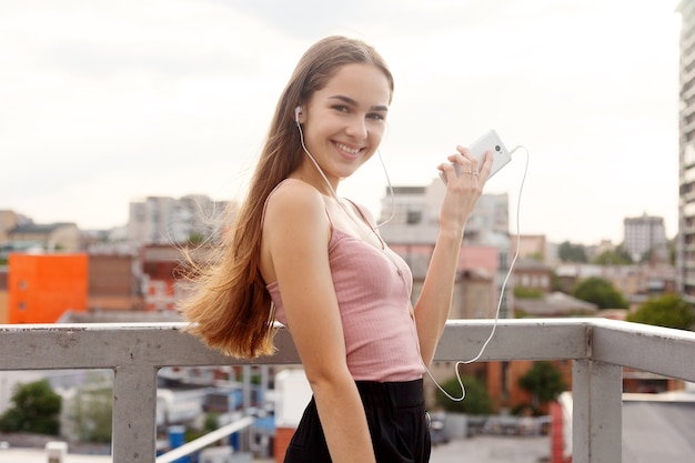 Mulher jovem com fones de ouvido pendurados em seu telefone celular enquanto caminha em uma rua urbana