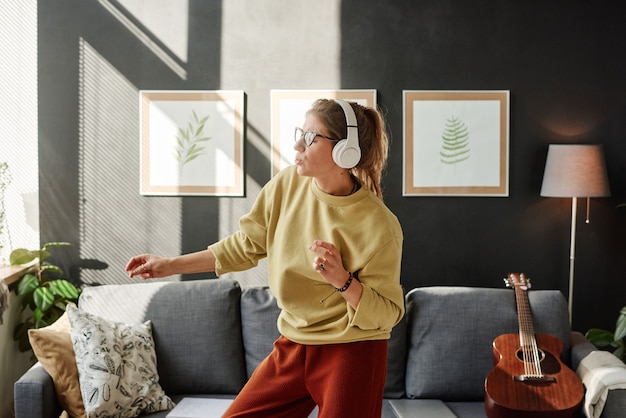 Foto mulher jovem com fones de ouvido sem fio, curtindo a música e dançando na sala de estar em casa