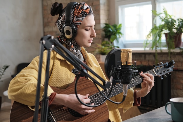 Mulher jovem com fones de ouvido tocando guitarra durante a transmissão no rádio