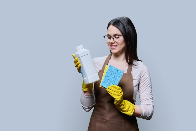 Mulher jovem com guantes de avental com detergente orgânico em fundo cinzento