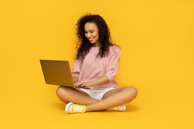 Mulher jovem com laptop em fundo amarelo