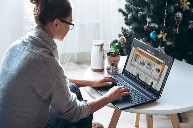 Mulher jovem com laptop no fundo de uma árvore de Natal