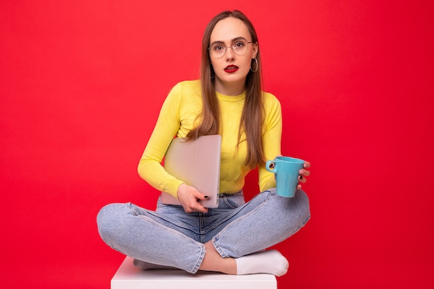 Mulher jovem com laptop tomando café sobre fundo vermelho